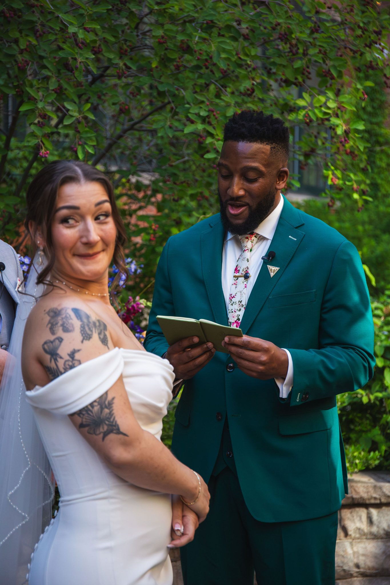 Chandler reading his vows to Gabrielle, who glances back with a playful smile