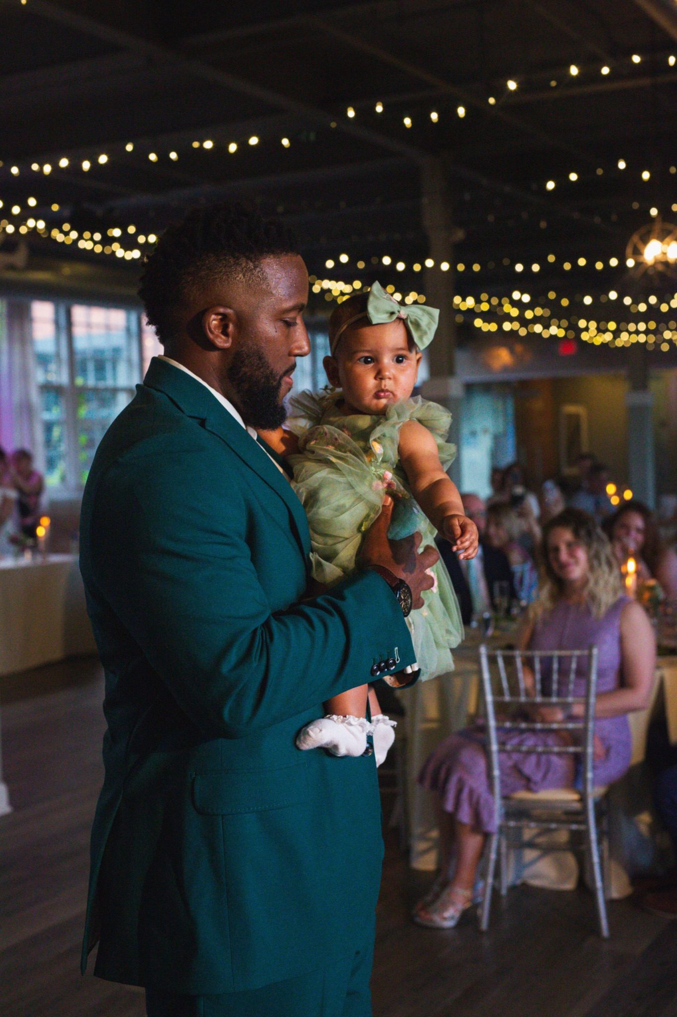 Chandler holding his baby daughter on the dance floor, string lights overhead