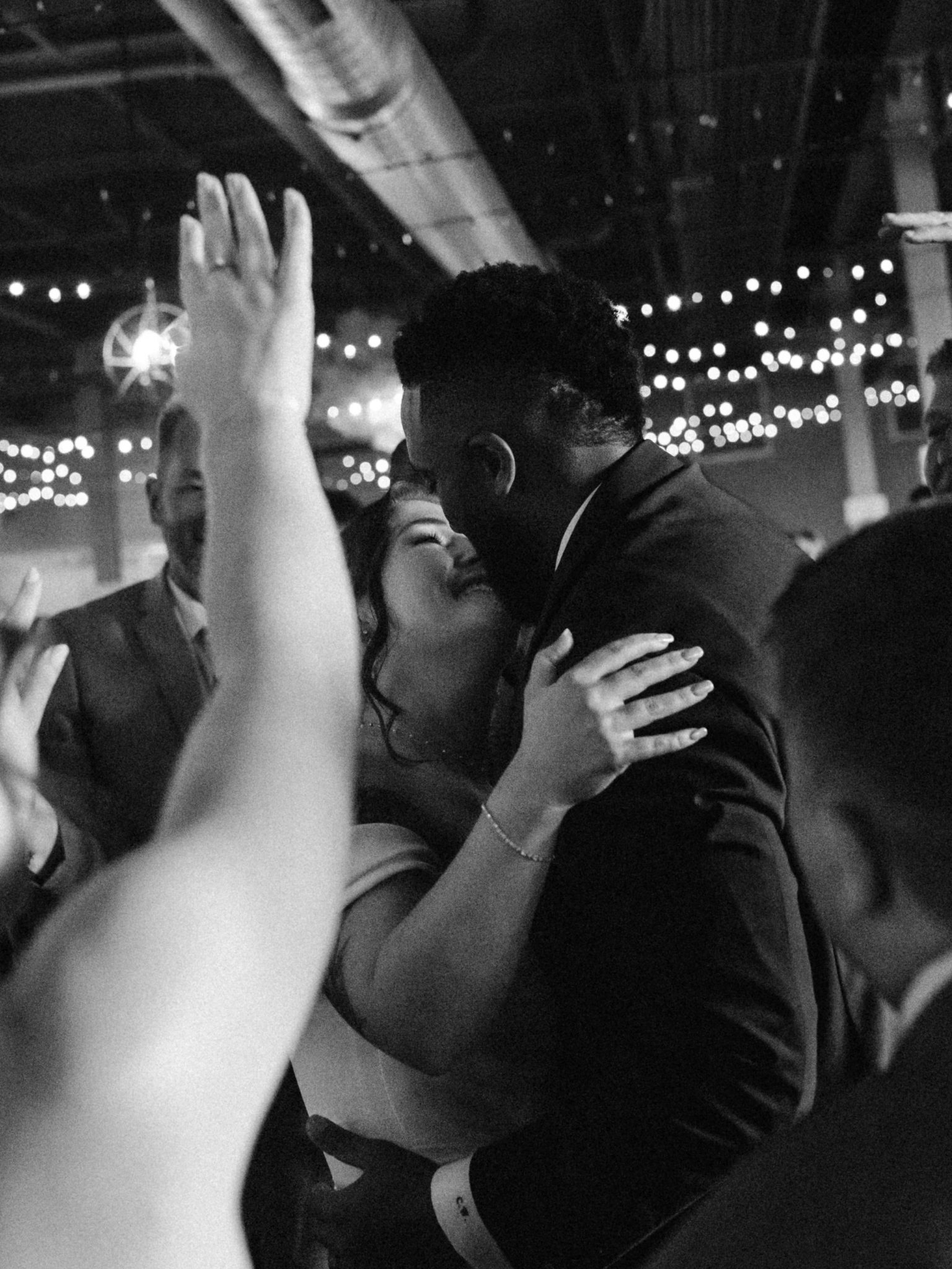 Black and white photo of Gabrielle and Chandler dancing closely, surrounded by guests