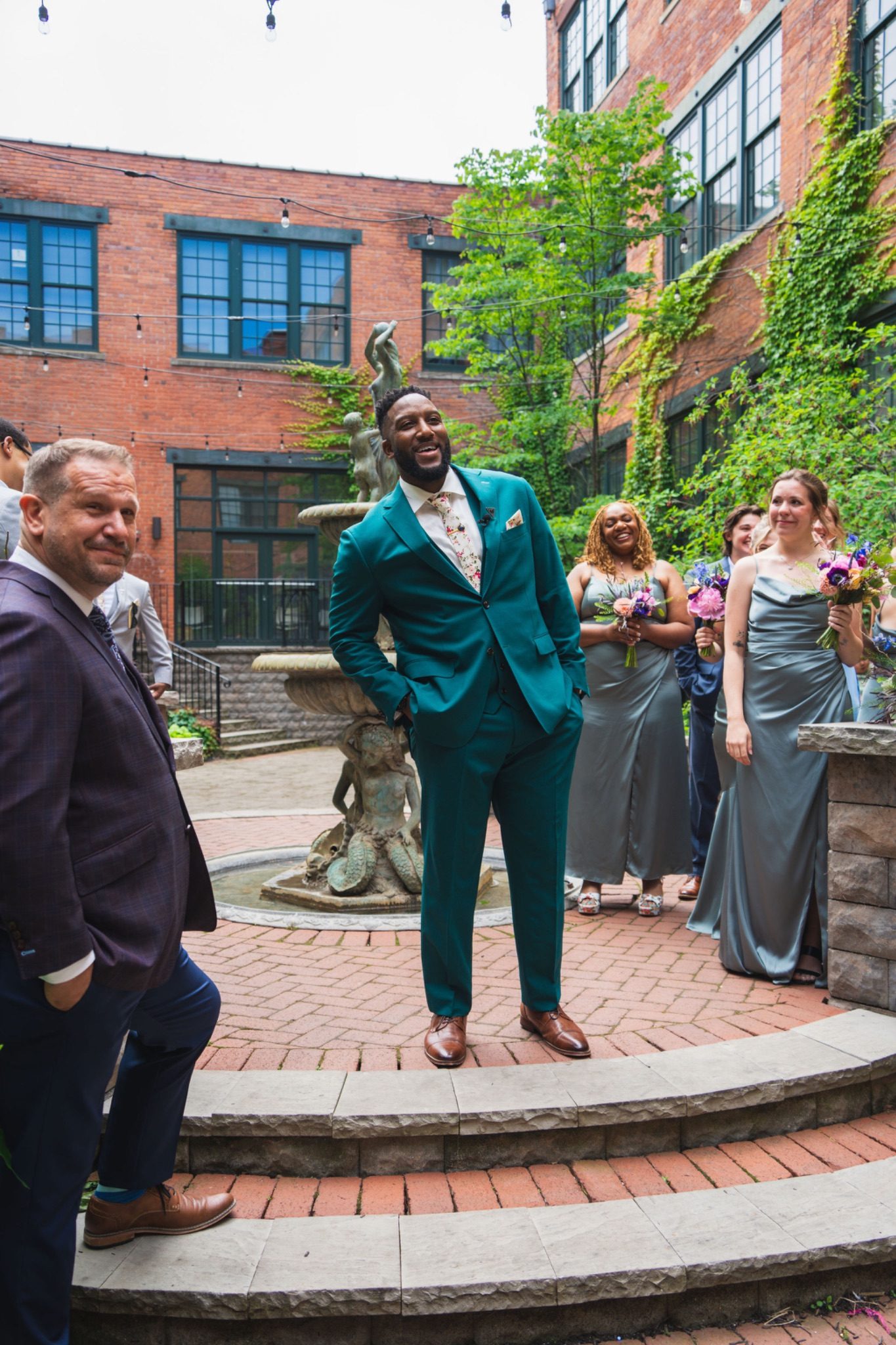Chandler and the bridal party reacting with joy in the courtyard fountain during the first look