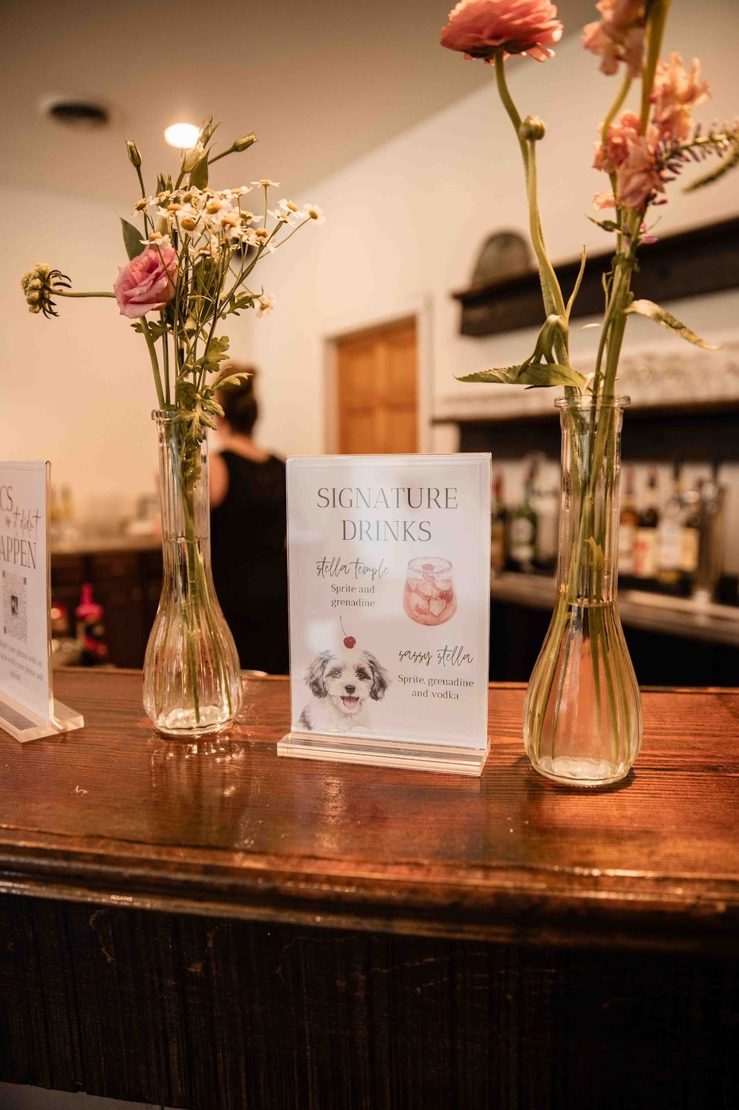 Signature drinks sign on the bar surrounded by bud vases of pink and white florals