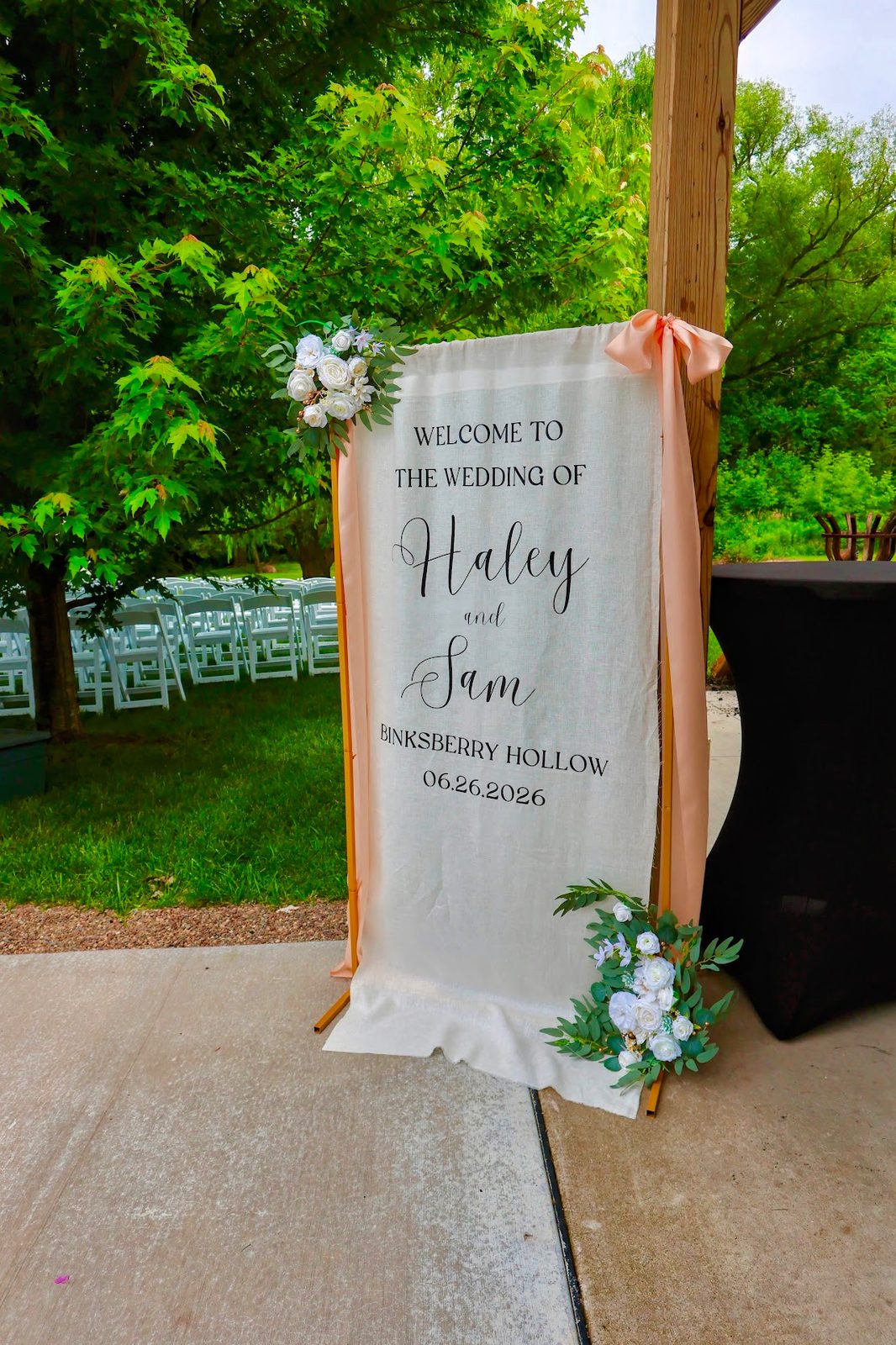 Welcome sign for Haley and Sam's wedding at Binksberry Hollow, dressed with peach ribbon and white florals