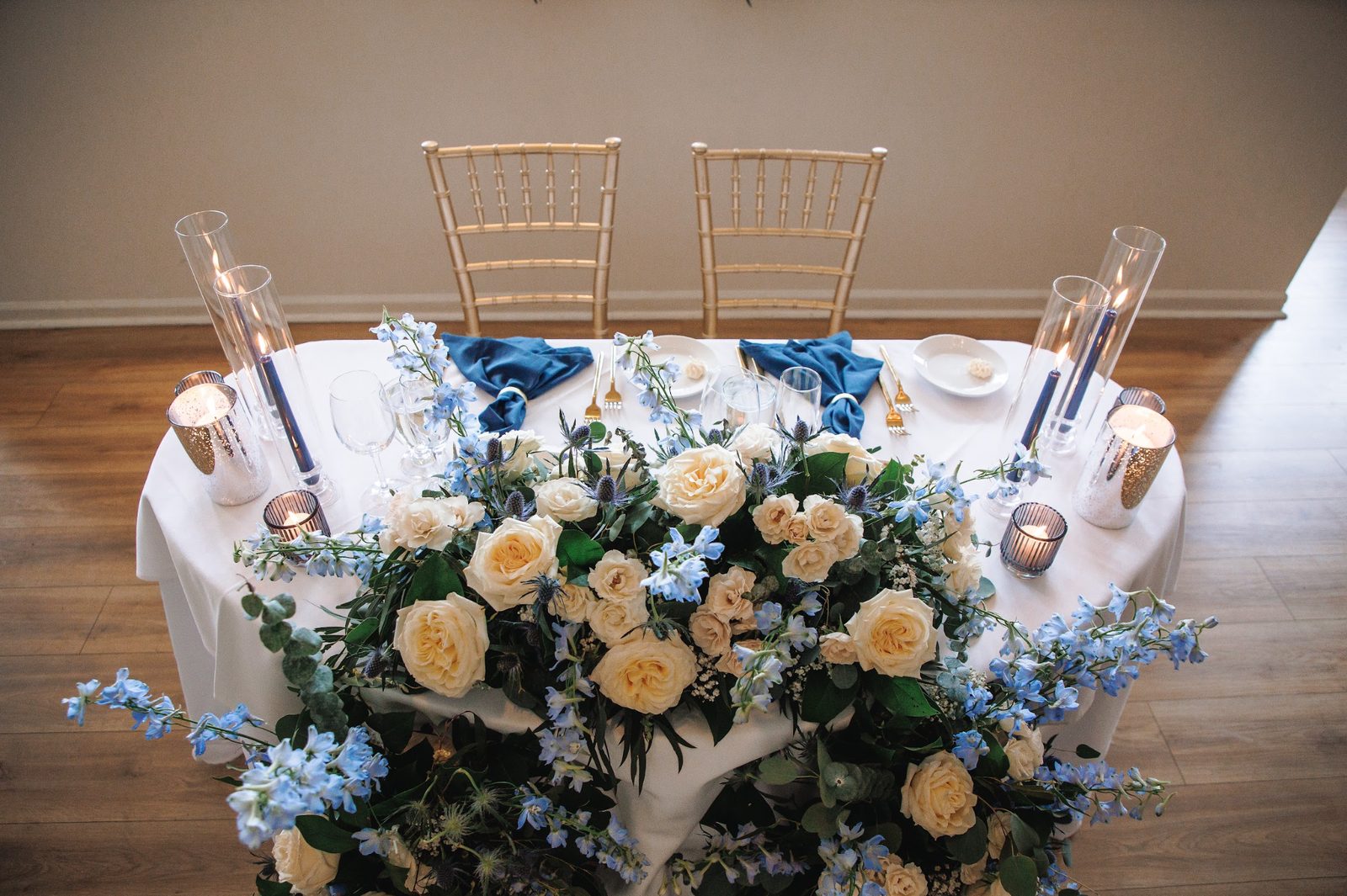 Sweetheart table with candlelight and ivory and blue florals in front of gold chiavari chairs