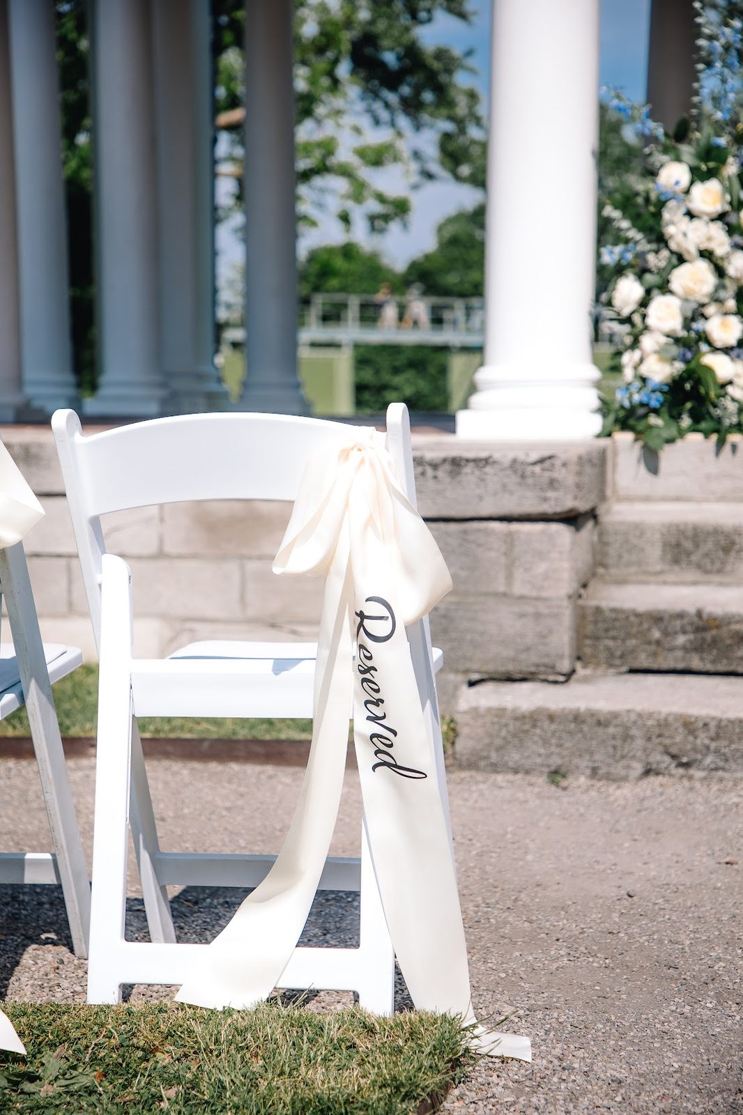 White ceremony chair with a Reserved ribbon in front of a floral-draped staircase